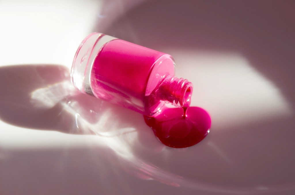 Pink nail polish dripping from its bottle under natural light, creating deep shadows